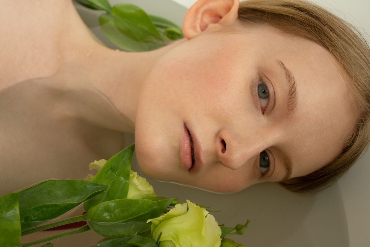 Close-up of a woman relaxing in a bathtub with greenery and flowers, creating a serene and tranquil mood.