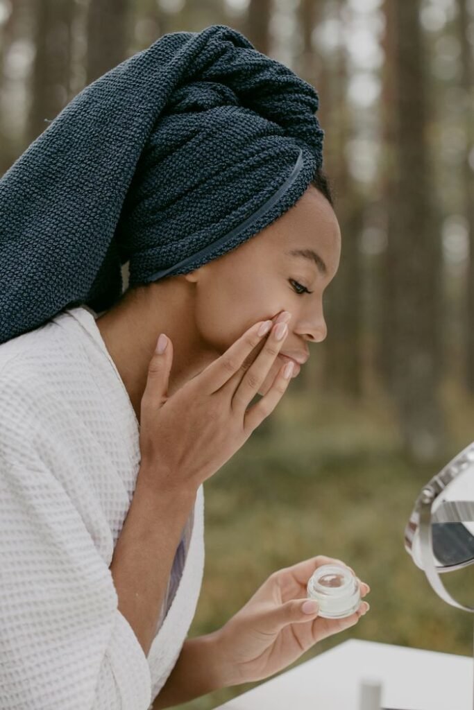 Woman enjoying a skincare routine in a forest setting, applying cream with serene focus.