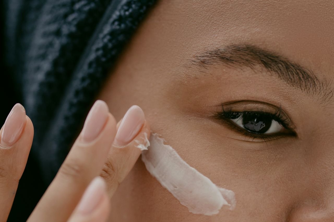 Extreme close-up of a woman applying cream to her cheek for healthy skin care.